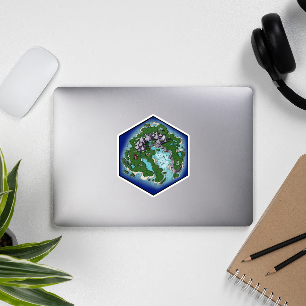 A hexagonal island treasure map illustration is a sticker on a laptop with common accessories around it for scale.