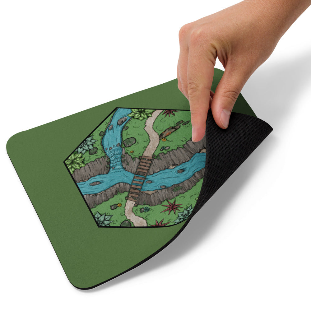 A hand pulls up the corner of the Perilous Crossing mousepad.