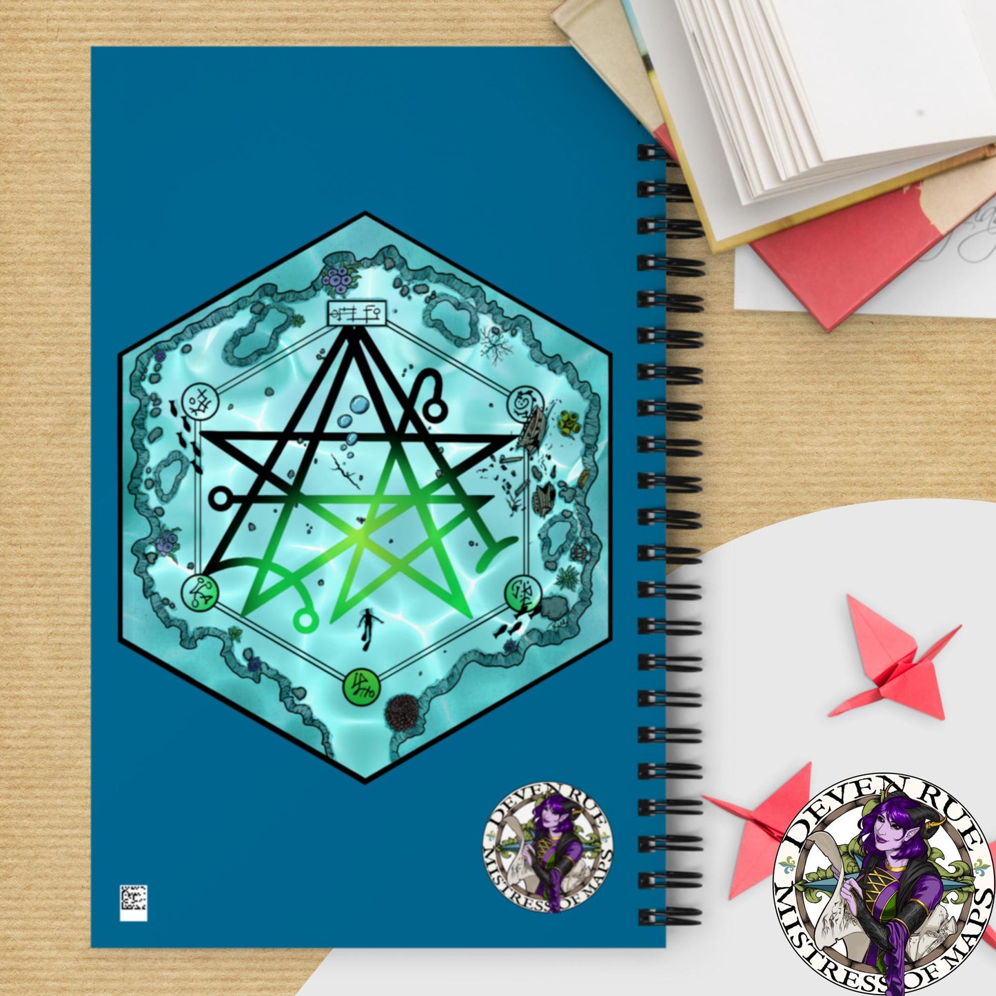A teal spiral notebook with the Discovering the Gate hex map and the Deven Rue logo on the back.