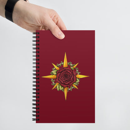 A hand holds a burgundy spiral notebook with the Druid Compass Rose illustration on the front.