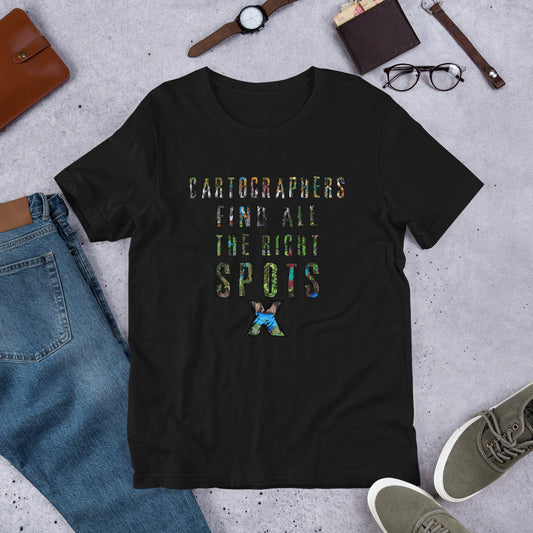 A black t-shirt sits on the ground with common clothes and accessories. Text on the shirt reads, "Cartographers find all the right spots" with a X and maps overlayed on the text.
