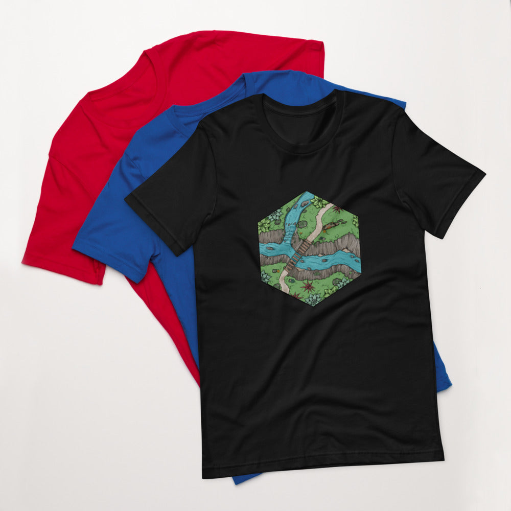 A black t-shirt with a small illustration of a river crossing. A blue and a red shirt sit under them.