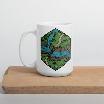 A mug with a hexagonal portion of a river crossing illustration sits on a wooden plank.