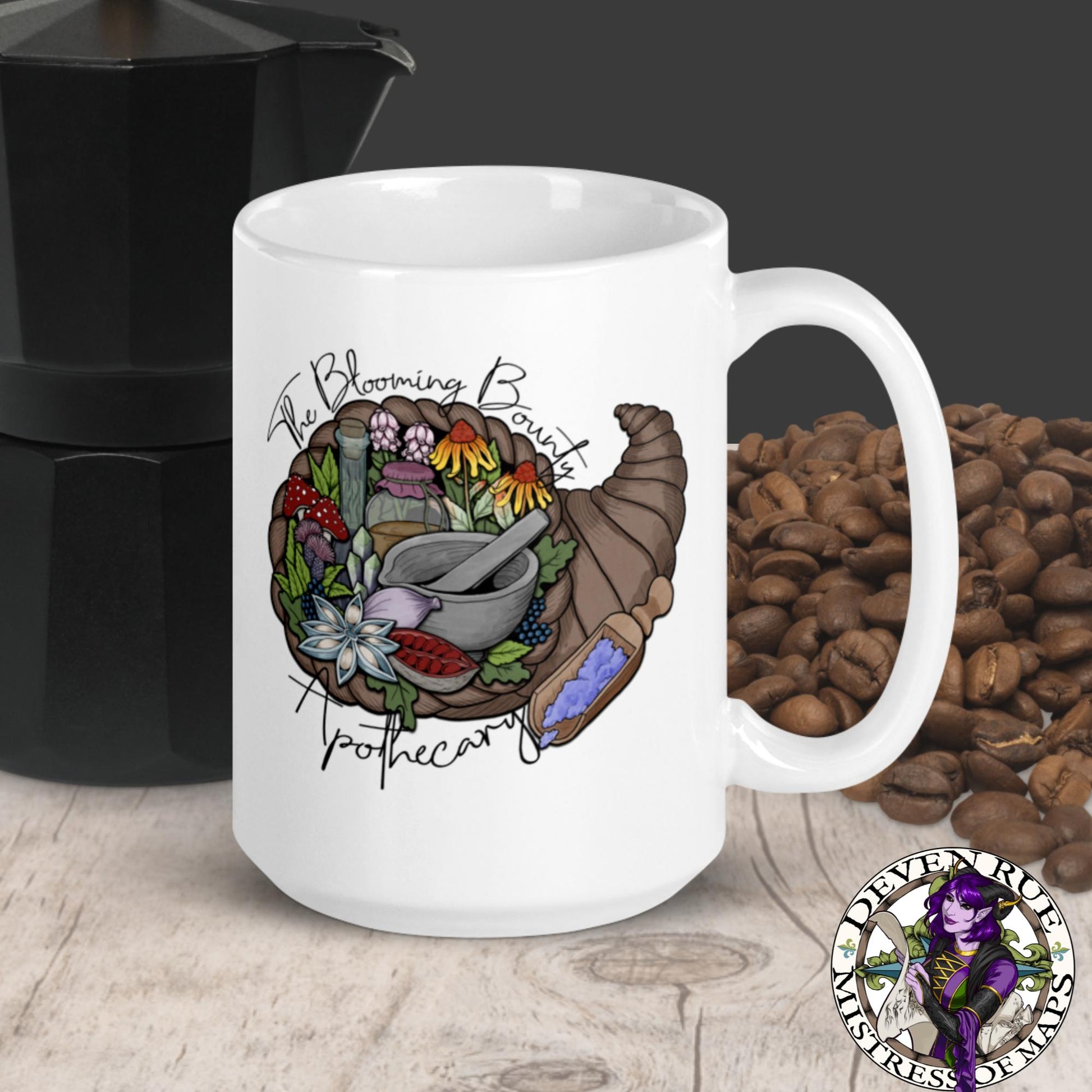 A white mug with The Blooming Bounty Apothecary logo featuring a cornucopia of herbalism supplies, sits with coffee beans and a kettle.